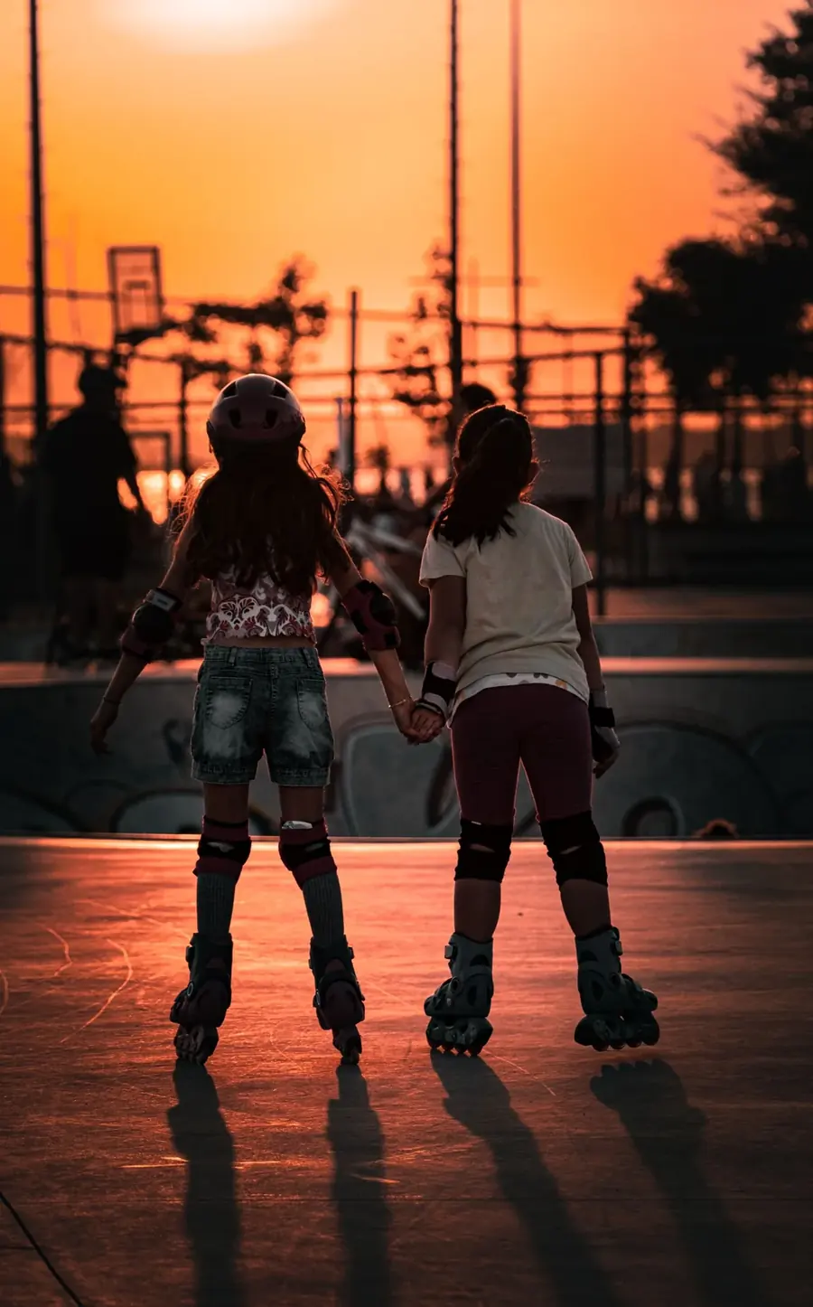 Dos patinadoras tomadas de la mano rodando hacia el atardecer