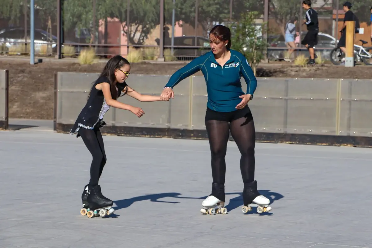 Instructora tomando de la mano a una niña que aprende a patinar